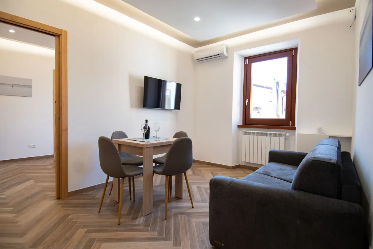 Soggiorno luminoso con zona pranzo, divano (anche letto), TV e aria condizionata. Atmosfera moderna e accogliente nel cuore del borgo.
